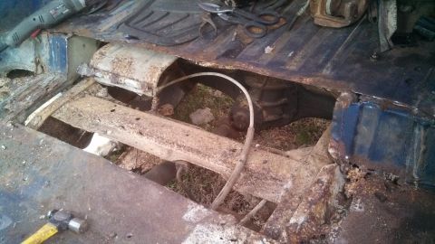 1979 Ford Bronco - This image shows the heavily rusted floor pan of a vehicle, with tools like a grinder and hammer visible, indicating repair or dismantling…