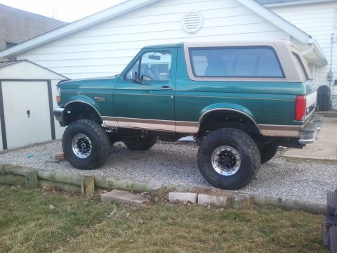 1996 Ford Bronco - A lifted 1996 Ford Bronco in green with a tan top sits on a gravel driveway next to a house.