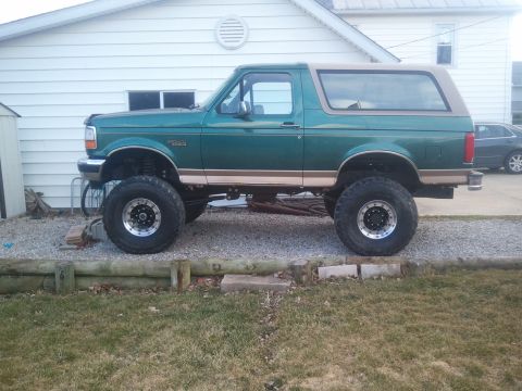1996 Ford Bronco - This lifted 1996 Ford Bronco features a two-tone paint scheme with a green body and tan top, complemented by aggressive off-road tires.