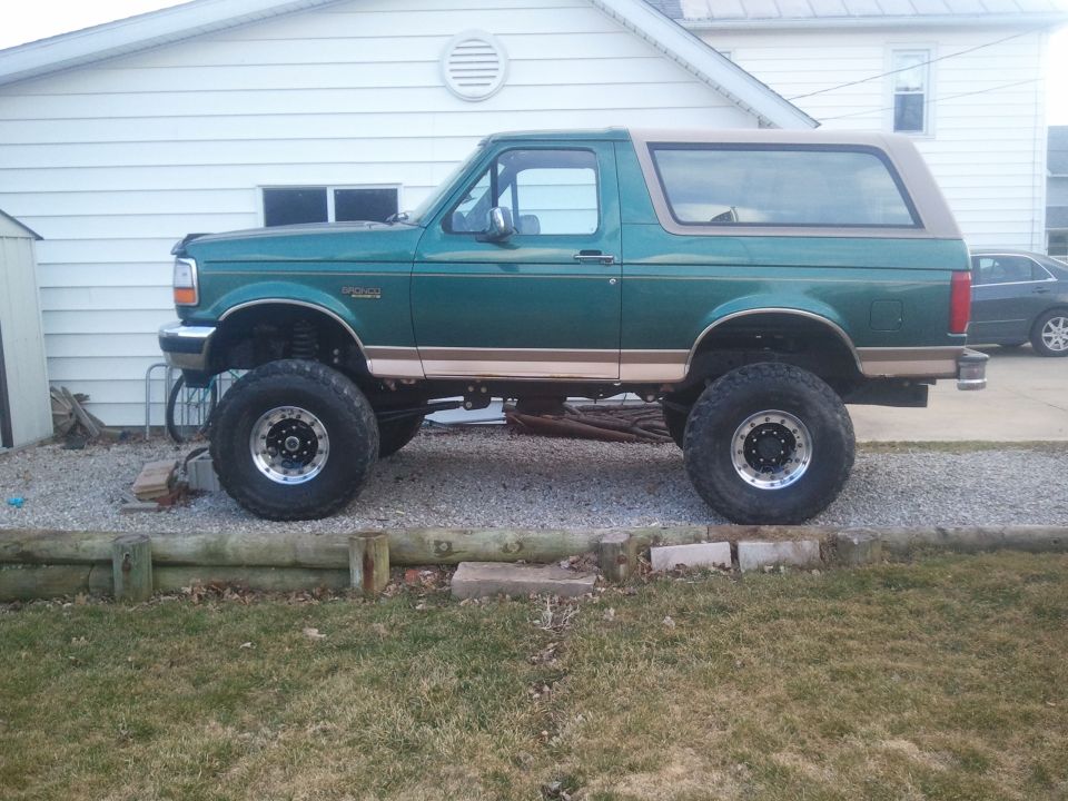 Side view of a lifted green 1996 Ford Bronco with a tan top and large off-road tires