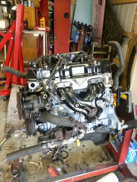 1987 Toyota 4Runner - Engine assembly on a red engine stand in a garage, with tools and parts scattered around.