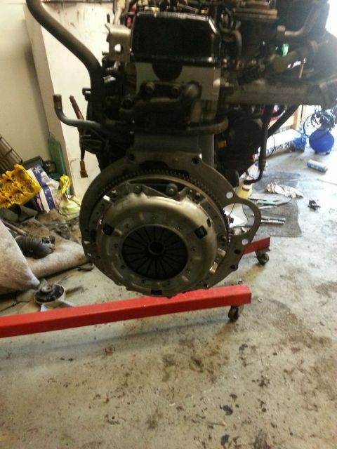 1987 Toyota 4Runner - Engine and transmission assembly on a red engine stand, with clutch visible. The background shows a workshop environment.