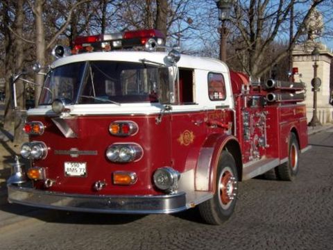 1991 Ford Crown Victoria - A red and white fire truck is parked on a cobblestone street with trees in the background.