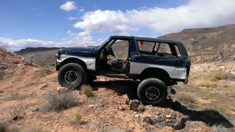 1994 Ford Bronco - Modified Ford Bronco parked on rocky desert terrain with doors open.
