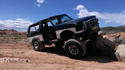 1994 Ford Bronco - A modified Ford Bronco navigates a rocky terrain under a blue sky.