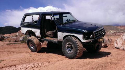 1994 Ford Bronco - This modified Ford Bronco sits on a dusty, rocky terrain under a cloudy sky.