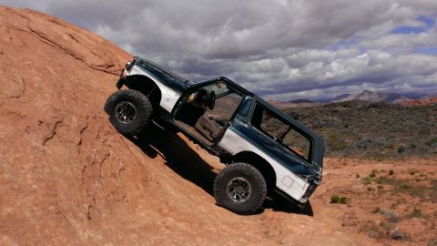 1994 Ford Bronco - An off-road SUV navigates a challenging rocky terrain under a dramatic sky.