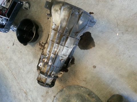 1994 Ford Bronco - A transmission part is shown on a concrete floor next to an oil pan, with some fluid spilled around it.