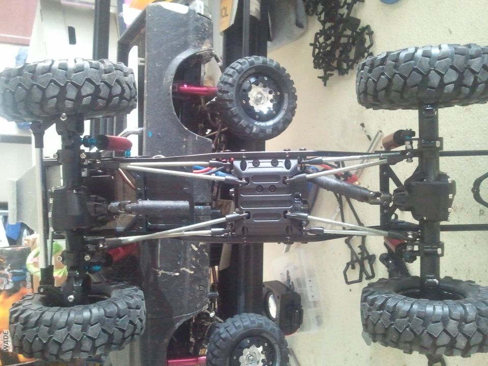 Upside-down off-road vehicle chassis with large tires and suspension components visible