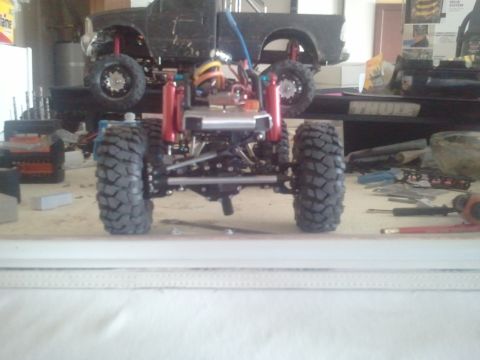 1985 Ford Bronco - A detailed view of a remote control truck's chassis and suspension system, with a larger truck body visible in the background.