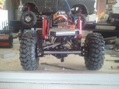 1985 Ford Bronco - The detailed chassis and large tires of a remote-controlled vehicle are shown from the rear, with another RC vehicle in the background.