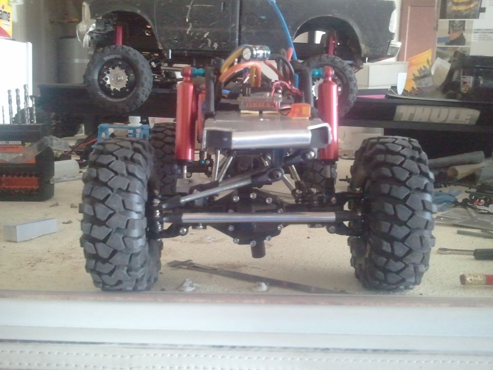 RC car chassis with large tires and red shocks, rear view. Another vehicle is visible behind
