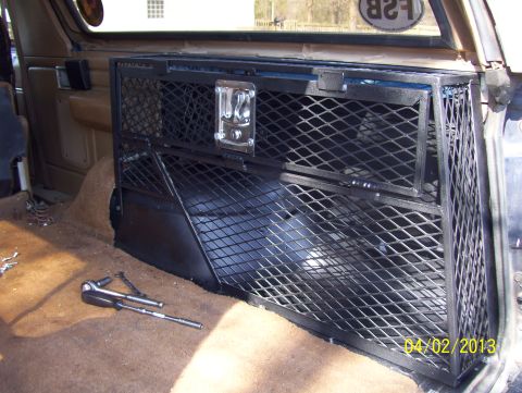1990 Ford Bronco - Interior view of a vehicle's rear storage area, a custom metal cage and tools on the carpeted floor.