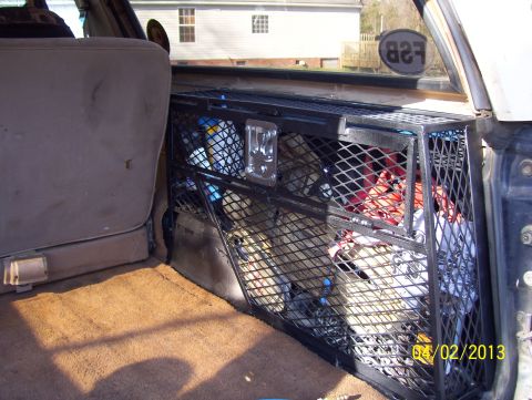 1990 Ford Bronco - The rear storage compartment of a vehicle contains a metal cage holding various items, with a seat to the left.