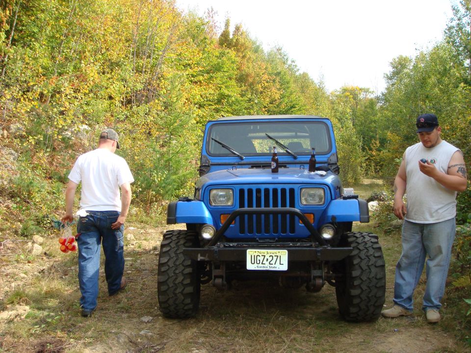 Blue Jeep Wrangler parked on a dirt road with two guys nearby