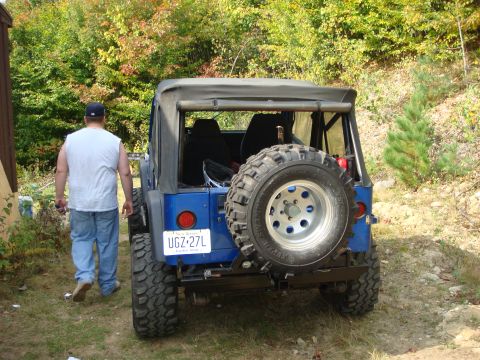 1990 Ford Bronco - A blue Jeep Wrangler is viewed from the rear, parked outdoors with a man walking away from it.