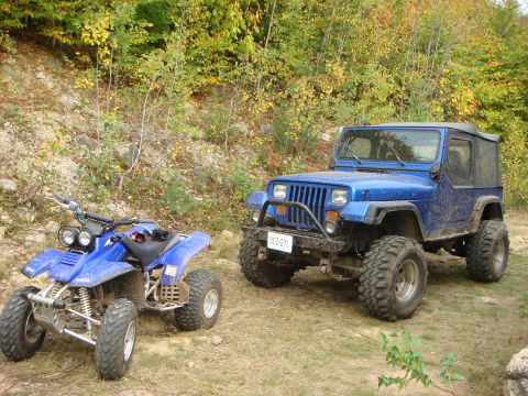 1990 Ford Bronco - A blue Jeep Wrangler and an ATV sit parked on a dirt path surrounded by autumn foliage.