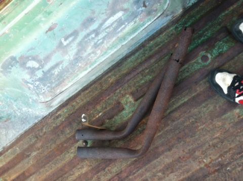 1977 Ford F-350 - Two rusty exhaust pipes lie on the corrugated metal bedliner of a vehicle, with a portion of a shoe visible on the right.