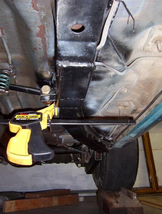 Fabricated steel bracket clamped under a car floorpan during test fitting in a garage