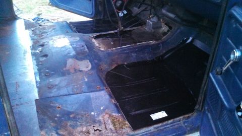1979 Ford Bronco - The interior of a blue vehicle shows significant rust on the floorboards, with a new black panel being installed.