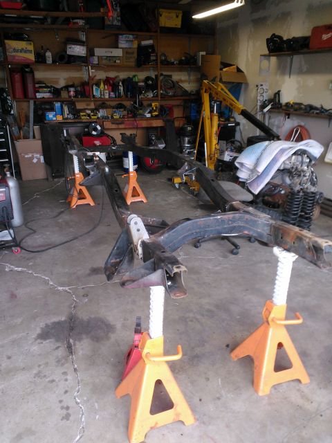 1968 Ford Bronco - Vehicle frame assembly undergoing work in a garage setting, with various tools and parts in the background.