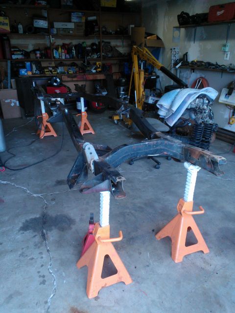 1968 Ford Bronco - The chassis and engine of a vehicle are disassembled and supported by jack stands in a workshop.