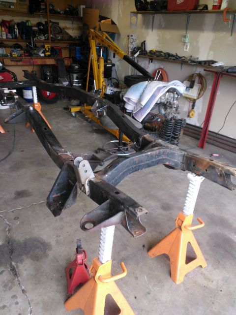 1968 Ford Bronco - A vehicle frame is supported by jack stands in a garage, with an engine and hoist visible in the background.