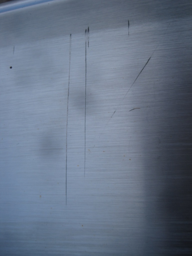 Close-up of a brushed metal panel with several long scratches and a small dark spot