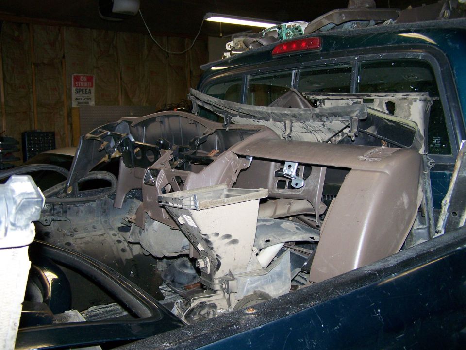 Disassembled dashboard and interior parts piled inside a dark green pickup truck cab