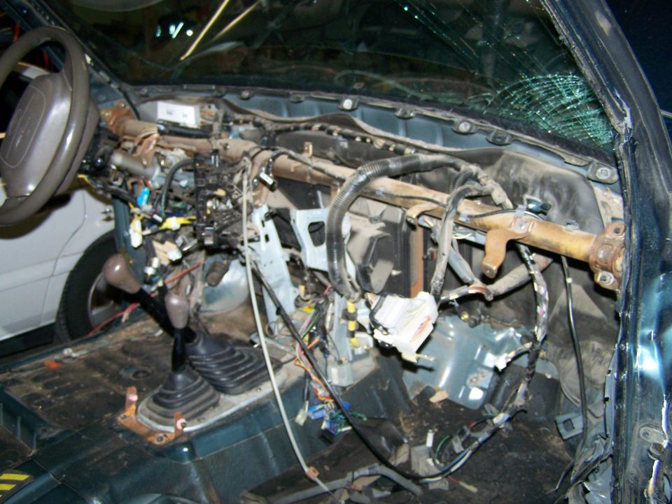 Disassembled dashboard and wiring harness of a vehicle, showing exposed components and a cracked windshield