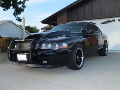 2003 Ford Crown Victoria - A black 2003 Ford Crown Victoria is parked in a driveway, a push bar and an aftermarket hood.