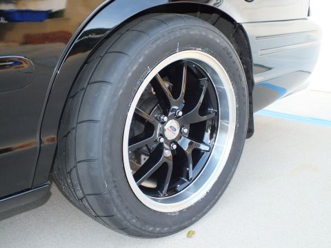 2003 Ford Crown Victoria - Close-up of the rear wheel on a black 2003 Ford Crown Victoria, a Ford badge on the hub.