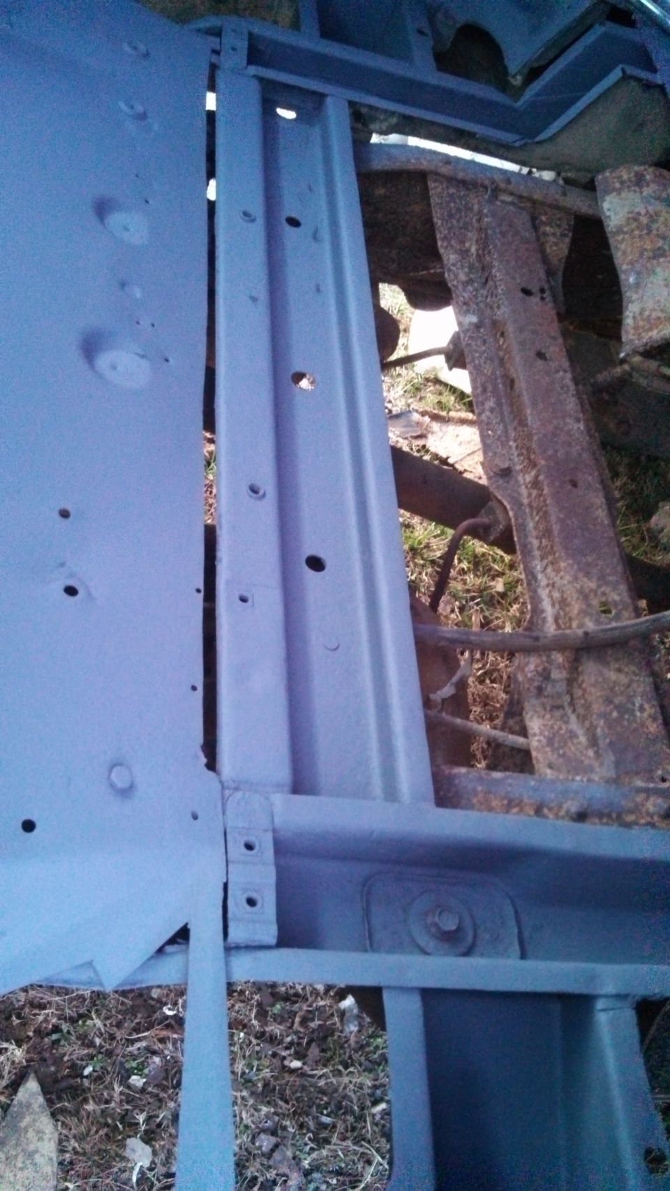 Blue painted vehicle frame and floor pan with rusty metal components visible