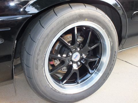 2003 Ford Crown Victoria - Close-up of a black performance wheel and tire on a black vehicle, a Ford logo on the center cap.