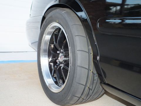 2003 Ford Crown Victoria - Close-up of a black car's rear wheel and tire assembly.