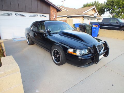 2003 Ford Crown Victoria - A modified black sedan with a prominent hood scoop and a front push bar sits in a driveway.