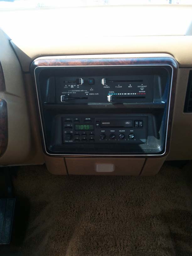 Dashboard with wood trim, climate controls, and a Ford radio displaying 107.9
