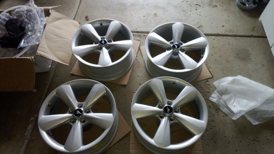 Set of four silver five-spoke Mustang alloy wheels with pony center caps on garage floor