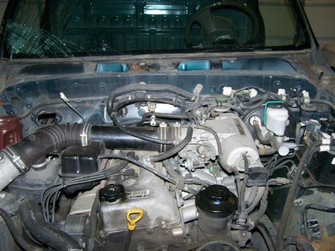 1988 Suzuki Samurai - The engine bay of a vehicle shows various components, with a cracked windshield visible above.