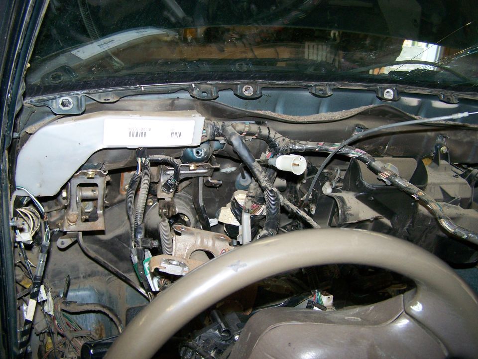 Interior dashboard wiring and components with a beige steering wheel visible