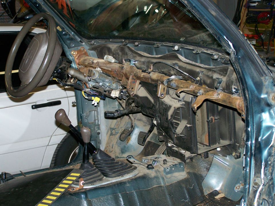 Disassembled dashboard and steering column of a vehicle, showing exposed wiring and metal framework