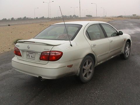 2004 Nissan Maxima - A white Nissan sedan is parked on a wet road, showing its rear and side profile.