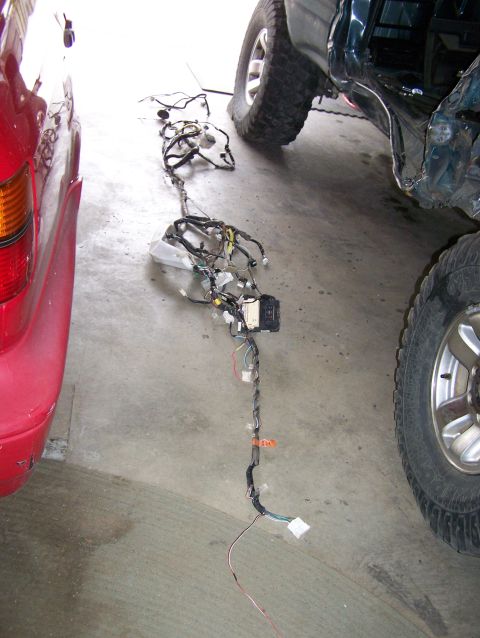 1988 Suzuki Samurai - A vehicle wiring harness is displayed on the floor, adjacent to a red car and a dark-colored SUV.