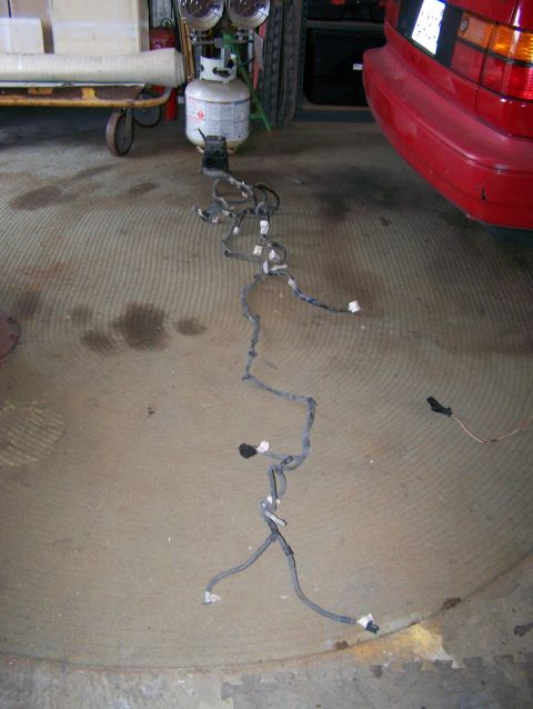 1988 Suzuki Samurai - A vehicle wiring harness is spread out on the floor, with the rear of a red car visible in the background.