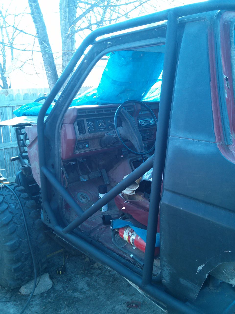 Roll cage inside a red and black Ford Bronco, dashboard visible, fire extinguisher on floor
