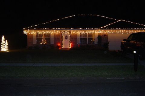 1993 Ford Bronco - A suburban house is adorned with festive Christmas lights, including icicle lights and a glowing tree on the lawn.
