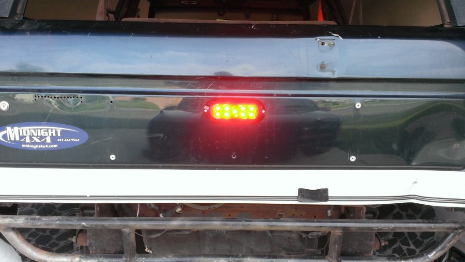 Dark tailgate of a Ford Bronco with a blue 'Midnight 4x4' sticker and a red LED brake light