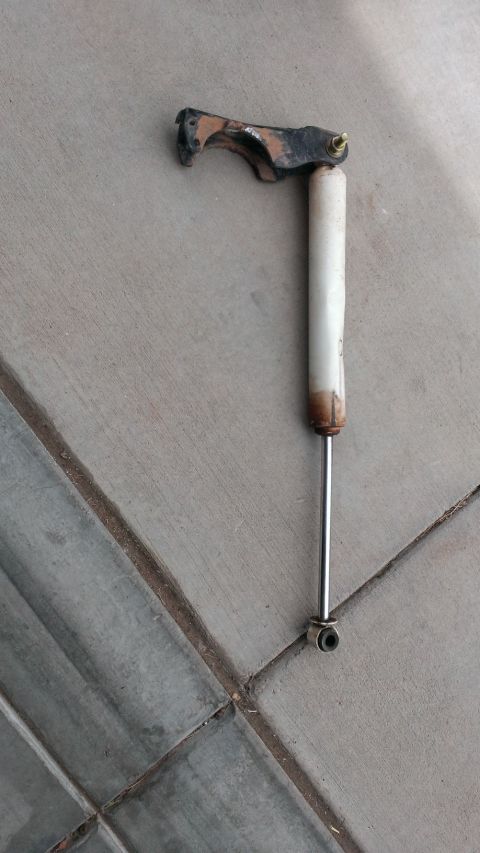 1994 Ford Bronco - A shock absorber with its mounting bracket is shown lying on a tiled surface.