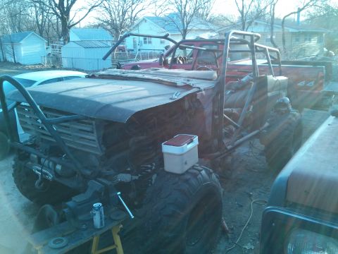 1986 Ford Bronco - Custom off-road build with extensive roll cage and large tires, parked outdoors with another vehicle in the background.