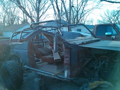 1986 Ford Bronco - This custom vehicle appears to be undergoing significant modification for off-road use, with a prominent roll cage and stripped-down body.
